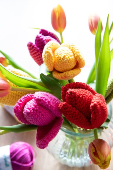Un bouquet de tulipes en crochet colorées dans un vase transparent.