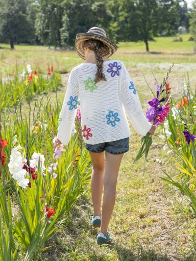 Jeune fille portant un pull fait main au crochet à fleurs colorées et shorts, au milieu de fleurs.