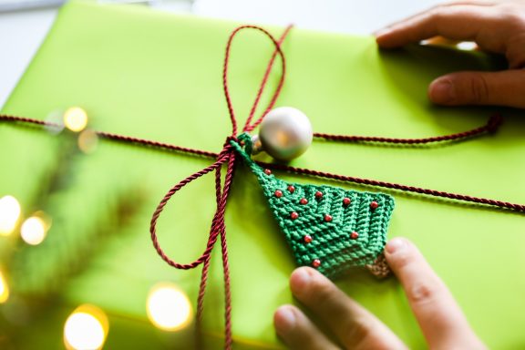 Cadeau vert avec un décor de sapin et une boule, tied avec un ruban rouge.