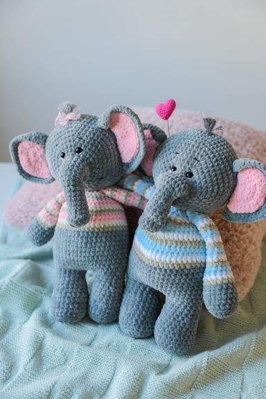 Deux éléphants en peluche en crochet, l'un rayé rose et l'autre bleu, assis ensemble.