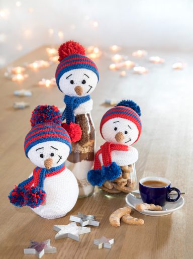 Trois bonhommes de neige en décoration avec des pompons rouges et bleus autour d'une tasse de café.
