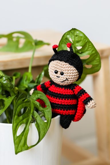 Amigurumi en crochet en forme de coccinelle sur un pot de plante verte.