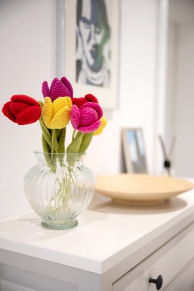 Un vase avec des tulipes roses, jaunes et violettes au crochet sur une table.